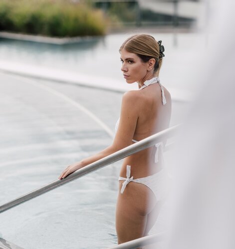 Blonde Dame in weißem Bikini steigt in das Kaskaden-Becken der Therme im Spa Resort Geinberg | © Spa Resort Geinberg / Chris Perkles