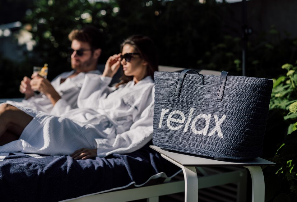 Paar entspannt auf einer Liege im Relax! Garten, daneben eine Relax! Badetasche | © Spa Resort Geinberg / Chris Perkles