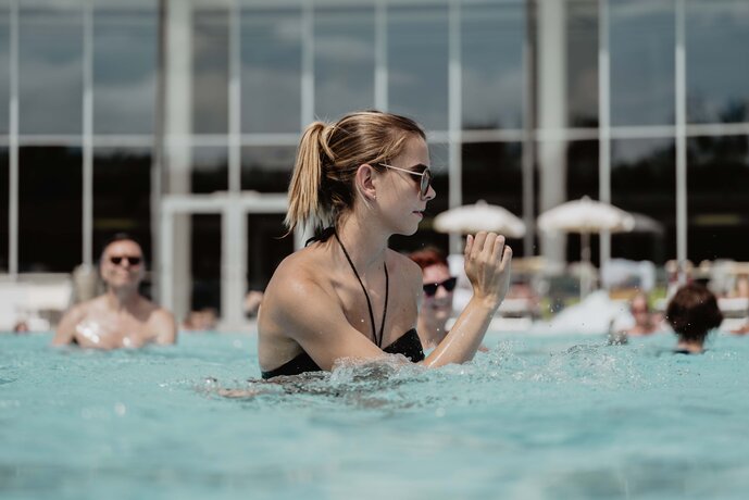 Blonde Frau mit Sonnenbrille nimmt engagiert am Aqua Fitness Kurs des Spa Resort Geinberg teil | © Spa Resort Geinberg / Chris Perkles