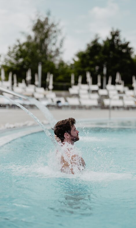 Mann genießt das Wasser unter der Schwalldusche im Thermal-Becken des Spa Resort Geinberg | © Spa Resort Geinberg / Chris Perkles